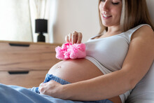 Baby Shoes Pregnancy Woman. Beautiful Pregnant Woman Holding Pink Baby Shoes. Concept Of Pregnancy, Maternity, Expectation For Baby Birth.