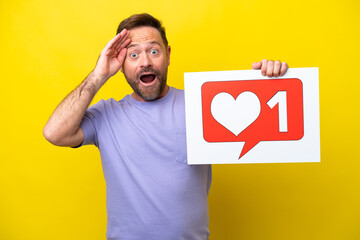 Middle age caucasian man isolated on yellow background holding a placard with Like icon with surprised expression