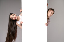 Surprised Teenagers Peeking Out At Edge With Copy Space. Portrait Cute Girl And Guy Looking At Camera Against A Gray Wall Studio. Childish Fashion And Happy Emotions Concept Of Caucasian Teenagers