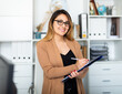 Young colombian woman manager in glasses holding clipboard in modern office