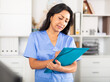 © JackF - Positive brunette woman doctor standing in office with clipboard in hands, writing medical history sheet