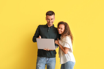 Wall Mural - Young couple using laptop on yellow background