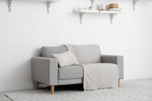 Grey Sofa With Pillows, Plaid And Shelves Hanging On Light Wall