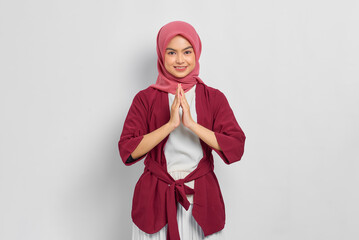 Wall Mural - Smiling beautiful Asian woman in casual shirt gesturing eid mubarak greeting isolated over white background