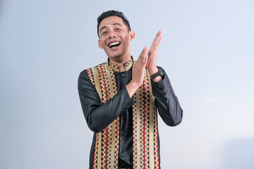 Portrait of an Asian man wearing a woven combination shirt with a happy gesture and expression on a gray studio background