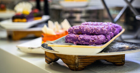 Wall Mural - Eclairs with sweet purple topping with nuts on serving plate