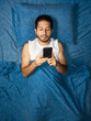 © Narayan - latin man using cell phone on blue bed, cell phone concept
