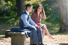 Young Couple Sitting On A Bench In The Park Talking