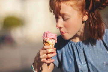 Wall Mural - Cute girl eating ice cream on summer background outdoors. closeup portrait of adorable redhaired little girl eating ice cream.