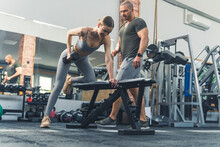An Attractive Caucasian Young Adult Woman Using Free Weights At A Fitness Facility To Build Up Her Upper Body Strength Under The Guidance Of Her Male Private Personal Trainer. High Quality Photo