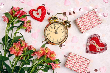 Wall Mural - Golden alarm clock with gifts, alstroemeria flowers, hearts and confetti on light marble table.