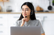 © kucherav - Asian female call center agent with headset working remotely from home on support hotline. Portrait of young woman help desk worker