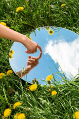 Wall Mural - nature concept - hand touching sky reflection in round mirror on summer field