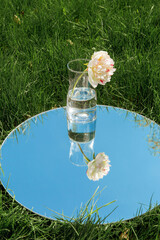 Wall Mural - nature concept - peony flower in glass vase and sky reflection in round mirror on summer field