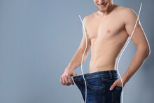 Happy Young Man With Slim Body In Oversized Jeans On Grey Background, Space For Text. Weight Loss