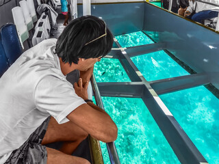 Male tourist looks at coral reefs through the transparent bottom of a ship in Sharm El Sheikh, Egypt. Tourist service of the exploration of the underwater life of the Red Sea from the submersible