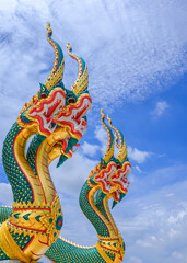 Low angle and side view of 2 colorful 3-headed serpent statues against white clouds on blue sky background in vertical frame