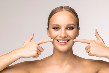 Wall Mural - Young woman with perfect skin, bright spring pink make-up and naked shoulders on a white background. Pointing fingers at snow-white teeth.