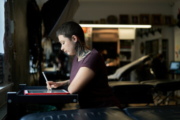 Sticker - Caucasian tattoo artist sitting at the studio and making new project