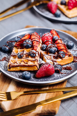 Wall Mural - Belgian waffle with chocolate, strawberry, blueberries and powdered sugar on dark plate