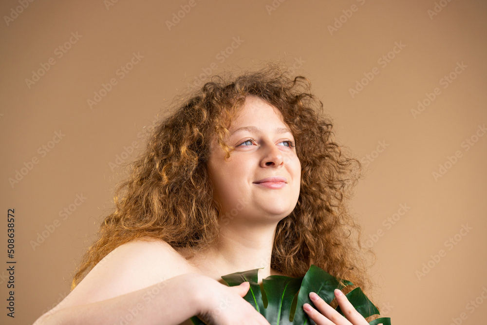 Woman holding a big green leaf covering her naked breast over an orange ...