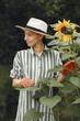 Woman in a hat and gloves standing near sunflowers