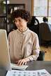 © pressmaster - Young woman in eyeglasses with curly hair sitting at her workplace at office and typing on computer keyboard