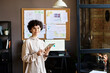 © pressmaster - Portrait of young businesswoman with curly hair smiling at camera while working on digital tablet at office