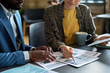 © pressmaster - Close-up of multiethnic business couple sitting at table together and discussing financial graphs on documents at office