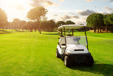 Golf Cart In Fairway Of Golf Course With Green Grass Field With Cloudy Sky And Trees At Sunset