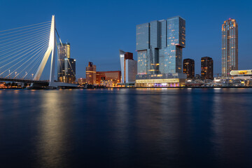 Wall Mural - Rotterdam nighttime panorama with “Erasmus-Bridge“ over river Nieuwe Maas at evening blue hour in South Holland Netherlands. Waterfront with illuminated bridge and tall buildings on the waterfront.