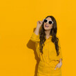 Young woman in linen shirt and shorts posing in sunglasses against yellow wall.