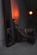 © NASTYA PALEHINA - teen fashion. young girl in shiny silver bodysuit is sitting fashion with closed eyes near mirror on floor with hands on knees on a gray loft wall background in red light. fashion concept, free space