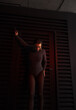 © NASTYA PALEHINA - teen fashion. young brunette girl in a shiny silver bodysuit and boots is standing fashion with hand up and looking down near black iron wall background with red light. fashion concept, free space