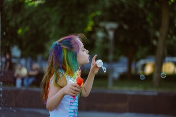 Wall Mural - caucasian cute little girl is blowing a soap bubbles in park. Image with selective focus