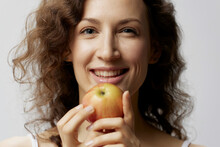 Closeup Portrait Of Cheerful Cute Curly Beautiful Woman In Basic White T-shirt Enjoy Apple Smiling Posing Isolated On Over White Background. Natural Eco-friendly Products Concept. Copy Space