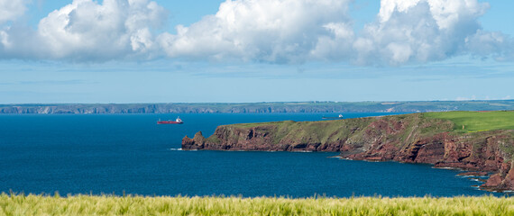 looking across a large blue estuary with a rocky headland under a blue sky with white cloud