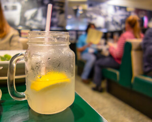 mug or glass of iced lemonade, with a straw, on a table in a bar or restaurant with blurred people and background