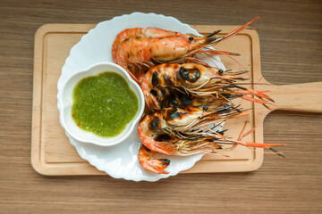 Burned river shrimp, grilled shrimp with spicy green chili seafood sauce in white plate on wooden table