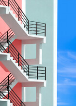 Side View Of White Fire Escape Outside Of Colorful Pastel Apartment Building With Blue Sky Background In Vertical Frame