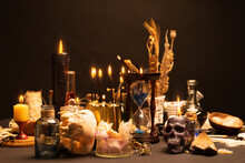 Occult And Esoteric Witch Doctor Still Life. Selective Focus. Halloween Background With Magic Objects. Black Candles Skull, Crystal Stones, And Potions Vials On Witch Table. Mystic Witchery With Weeds