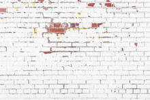 A Weathered And Distressed, White Brick Wall With Red Bricks And Yellow Paint Coming Through.
