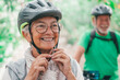 © Daniel - Portrait of one old woman smiling and enjoying nature outdoors riding bike with her husband laughing. Headshot of mature female with glasses feeling healthy. Senior putting on helmet to go trip