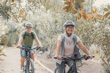 Canvas Print - Two happy old mature people enjoying and riding bikes together to be fit and healthy outdoors. Active seniors having fun training in nature.