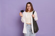 © sementsova321 - Portrait of pleased kind adorable woman with black bag wearing white shirt and jeans posing isolated over purple background, holding credit card in hands, banking.