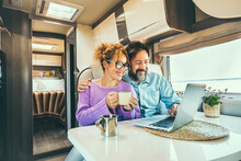 Modern Couple Use Together Laptop Inside Camper Van. Computer Leisure People Surfing The Web. Traveler Planning Next Destination Smiling And Enjoying Freedom Living Off Grid. Digital Nomad Concept