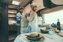 Happy Adult Couple Enjoy Vacation On Camper Van And Prepare Lunch Together. Alternative Travel Lifestyle For Modern People. Man And Woman Smile Inside Motor Home. Van Life And Holiday Trip Vacation