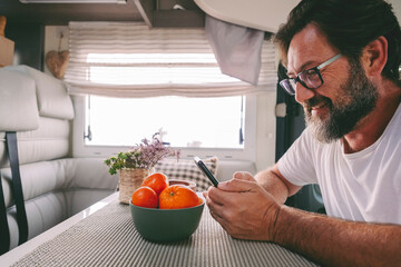 Wall Mural - Side portrait of mature handsome man using phone sitting on a camper van. People and travel lifestyle with everywhere connection. People communicate during travel road trip. Planning destination