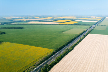 Agricultural land: Areas of various agricultural fields from a great height: green, yellow fields are separated by a highway. Agriculture in an agrarian country - aerial drone shot of plantations.