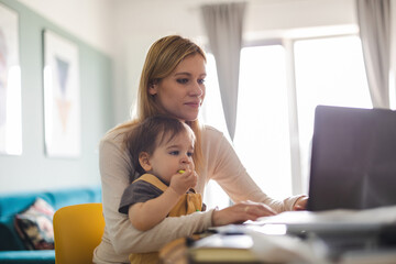 Mother working on laptop with child sitting on her lap 
